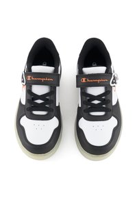 Baskets noires et blanches avec des panneaux en maille, bout rond, semelle rembourrée et une sangle en Velcro arborant un logo "Champion" orange.