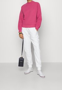 Felroze sweatshirt, witte joggingbroek met logo en witte sneakers. Accessoire: kleine zwarte handtas met een riem. Simpel ontwerp.