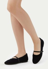 Svart kordflossa ballerinas med låg klack, med en dekorativ rem och cirkulär detalj. Slät textur och spetsig tådesign.