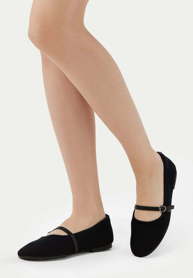 Svart kordflossa ballerinas med låg klack, med en dekorativ rem och cirkulär detalj. Slät textur och spetsig tådesign.