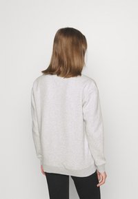 Sudadera gris con cuello redondo, mangas largas y puños de punto, que presenta una textura suave y un corte relajado. También son visibles pantalones negros.