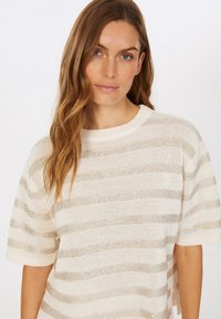 Cremfarbener Strickpullover mit metallischen goldenen Streifen, kurzen Ärmeln, runder Ausschnitt und leichten seitlichen Schlitzen. Strukturiertes Material mit feinem Schimmer.