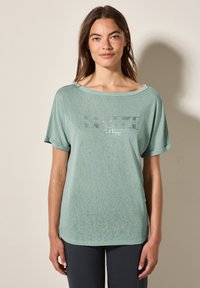 T-shirt mint vert à manches courtes avec un décolleté large, présentant un design graphique dans des couleurs contrastées. Matière douce avec une coupe décontractée.