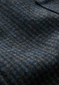 Wollstoff in Dunkelblau mit gr�ünen und gelben Sprenkeln, ausgestattet mit einer strukturierten Oberfläche und Hahnentrittmuster. Weich, warm und langlebig.