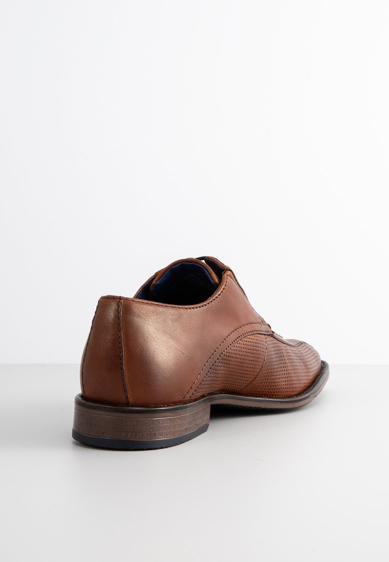 Zapato de cuero marrón con una textura suave, punta redondeada y detalles de diseño perforados. Presenta un tacón bajo y plano y una suela oscura.