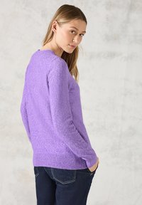 Maglione lavorato a maglia viola con finitura testurizzata, scollatura rotonda e polsini a coste. Abbinato a jeans blu scuro. Regolato per una vista laterale.