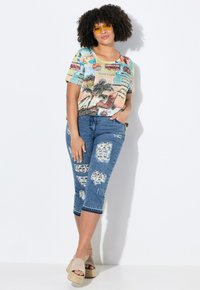 Kortærmet, farverig t-shirt med grafisk palmetrædesign, parret med slidte blå capri jeans og lysebrune platform sandaler.