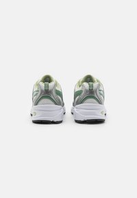 Tênis atléticos cinza e branco com detalhes em verde, parte superior em malha, colarinho acolchoado e solas em borracha, apresentando um laço distinto no calcanhar.