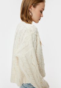 Pullover aus weichem, cremefarbenem Strick mit Zopfmustern und Perlenakzenten. Lässiger Schnitt mit geripptem Saum und lässigen Ärmeln.