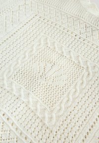 Tessuto lavorato a maglia color crema con motivi intricati, tra cui linee ondulate, forme a diamante e un motivo centrale a forma di mano.