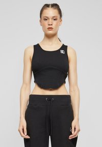 Must mustriba crop-top logodegusega, laiad rihmad ja tihe disain, koos mustade tõmblukkudega spordipükstega.