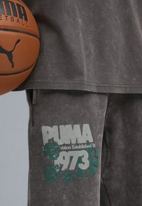 Grå bomuldsblanding sweatshirt med afrundet kant og et falmet design; parret med matchende grå sweatpants, der har et grønt grafisk logo og tekst.