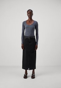 Temno siva oprijeta majica z dolgimi rokavi, kombinirana s črno denim midi krilo; krilo ima sprednji razporek in črni pas z zaponko. Celoten videz dopolnijo črne sandale.