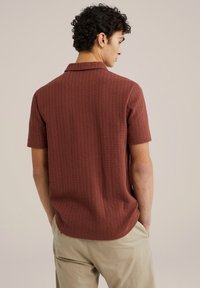 Kortærmet, rustfarvet polo skjorte med ribbet tekstur, en krave og en lige kant, parret med lyse beige bukser.