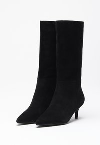 Bottines en daim noir avec un bout pointu et un talon fin. Texture lisse, tige haute, détails minimalistes et silhouette simple.