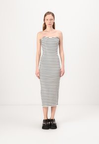 Vestido midi justo, sem alças, em branco com riscas horizontais pretas. Tecido suave e elástico, combinado com sapatos de plataforma pretos e chunky.
