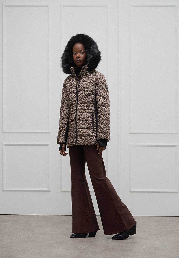 Leoprint-gefütterte Pufferjacke mit Kapuze aus Kunstfell, Reißverschluss vorne und schwarzen Seiteneinsätzen. Kombiniert mit braunen Hosen mit weitem Bein und schwarzen High-Heels.