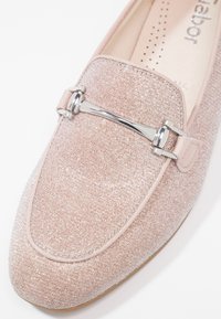 Mocassin rose clair scintillant avec détail en métal argenté en forme de mors de cheval à l'avant et bordure cousue autour de l'orteil.
