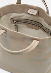 Tote en cuir beige avec deux poignées verticales, un extérieur lisse et un intérieur spacieux. Comprend une poche zippée et un logo de marque discret à l'intérieur.