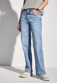 Jeans de mezclilla azul claro con un diseño de pierna recta, que cuentan con bolsillos delanteros y un clásico cierre de botones. Llevados con zapatillas blancas.