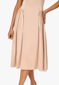 Knieumspielendes, ärmelloses Kleid aus weichem beigen Stoff mit gerafften Falten an der Taille und einem glatten, eleganten Design.