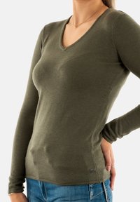 Haut ajusté à col en v à manches longues de couleur vert olive, fabriqué en matériau doux avec une texture subtile, présentant un petit logo de marque en bas.