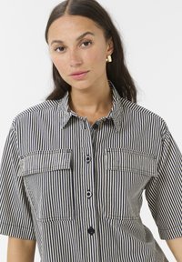 Chemise à rayures présentant des rayures horizontales bleu marine et crème, à manches courtes, avec deux poches poitrine et un col classique.