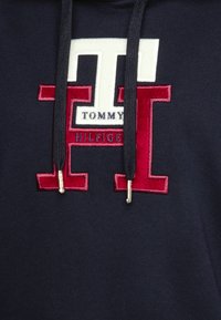 Námořnická mikina s velkým vyšitým oboustranným logem v červené a bílé barvě. Šňůrky s zlatými kovovými konci. Měkká textilní struktura.