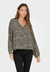 Maglietta a maniche lunghe con stampa zebra in beige e nero, caratterizzata da un scollo a V e una vestibilità comoda. Il tessuto appare leggero con una consistenza morbida.