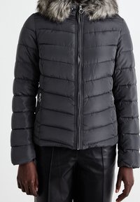 Pufferjack in donkergrijs met een met bont afgewerkte capuchon, gestikte textuur, twee zijzakken en een ritssluiting aan de voorkant.