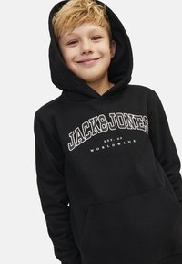 Black hoodie with a front pocket, large "JACK & JONES" text logo in white, adjustable hood, and soft fabric texture.