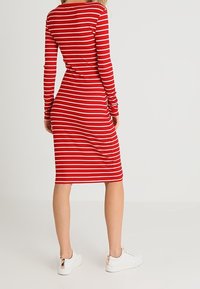 Punainen ja valkoinen raidallinen ribby pitkähihainen mekko, polvimittainen, kiinteä siluetti, parina valkoiset lenkkarit, joissa on ruusukultaiset korostukset.