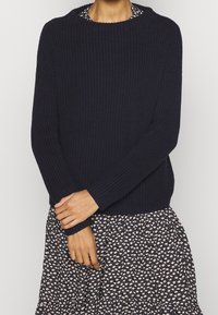 Granatowy sweter dzianinowy z prążkowaną fakturą i okrągłym dekoltem, zestawiony z wzorzystą sukienką w kwiaty z rozkloszowanym dołem.