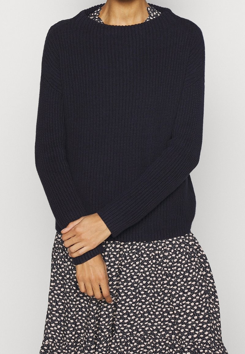 Granatowy sweter dzianinowy z prążkowaną fakturą i okrągłym dekoltem, zestawiony z wzorzystą sukienką w kwiaty z rozkloszowanym dołem.