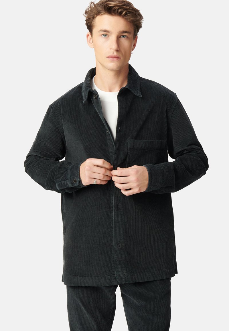 Giacca camicia in corduroy nera con vestibilità rilassata, chiusura frontale con bottoni, taschino sul petto e superficie testurizzata.