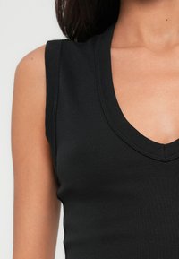 Haut noir sans manches avec un décolleté en V profond. Confectionné en tissu doux et extensible, avec une texture lisse et une silhouette ajustée.