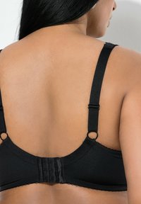 Kvinde set bagfra med justerbare sorte bh-stropper og hægte lukning på glat hud med langt mørkt hår.