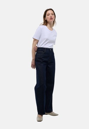 T-shirt blanc à manches courtes associé à un jean en denim bleu foncé taille haute, avec une coupe ample et un design classique à cinq poches.