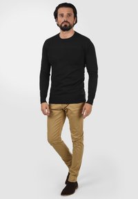Sort langærmet strikket sweater med rund hals, parret med lysebrune slim-fit bukser og mørkebrune ankelstøvler. Enkel, moderne design.
