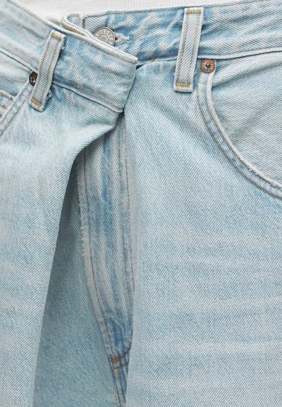 Világoskék farmernadrág, részben kigombolt derékrésszel, látható elülső zsebbel és övtartókkal.