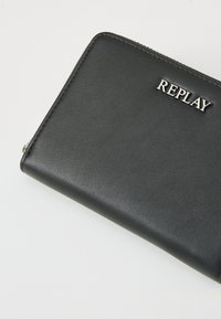 Zwart leren portemonnee met reliëf "REPLAY" logo, gladde textuur, ritssluiting en contrasterende stiksels langs de randen.