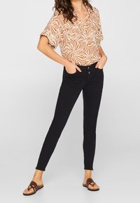 Pomarańczowo-biała koszula z krótkim rękawem w wzory, zestawiona z dopasowanymi czarnymi jeansami i brązowymi sandałami. Strój charakteryzuje się swobodnym fasonem.