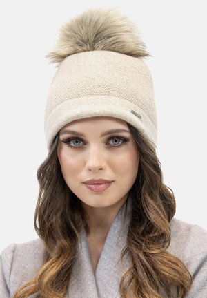 Berretto in maglia beige con un grande pompon in pelliccia sintetica, caratterizzato da un motivo testurizzato e un piccolo cartellino metallico sul lato.