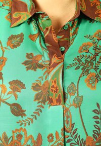 Green floral blouse featuring a brown collar, intricate leaf and flower patterns in orange and teal, with button details on the front.