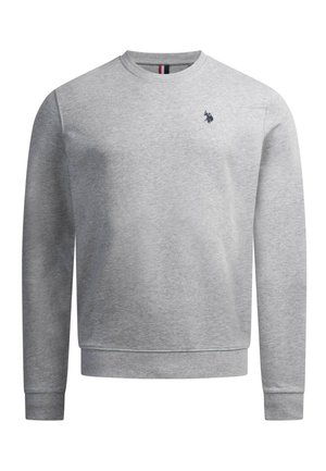 Man with dark hair and beard wearing a light grey sweatshirt with a small dark logo, standing with arms crossed against a plain background.
