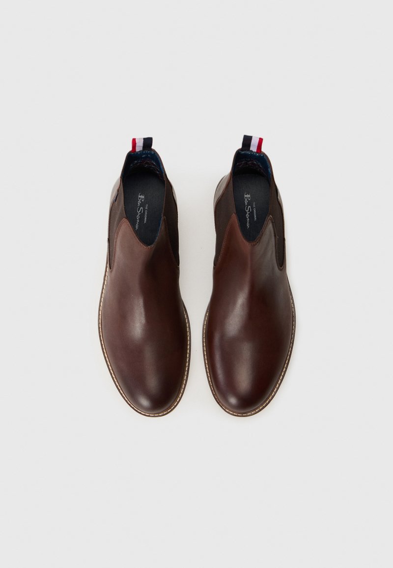 Chaussures en cuir marron à enfiler avec des panneaux élastiques sur les côtés, bouts ronds et un tirant décoratif au talon rouge, blanc et bleu.