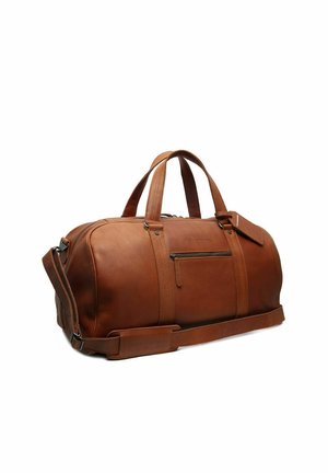 Bolsa de viaje de cuero marrón con asas dobles, bolsillo frontal con cremallera, correa de hombro ajustable y etiqueta de equipaje sobre fondo blanco.