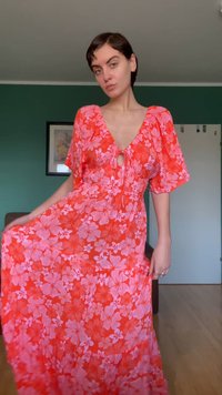 Κόκκινο μακρύ φόρεμα με κοντά μανίκια, με βαθύ V λαιμόκοψη και λεπτομέρεια με δέσιμο στη μέση. Ελαφρύ ύφασμα με ροζ λουλουδένια σχέδια.