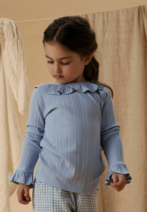 Light blue ribbed long-sleeve top with a ruffled neckline and flared cuffs, paired with checkered blue pants. Soft fabric and relaxed fit.