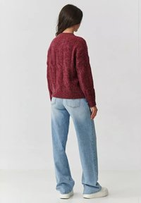 Burgundowa sweter dzianinowy o fakturze z okrągłym dekoltem, w połączeniu z jasnoniebieskimi szerokimi spodniami i białymi sneakersami na platformie.